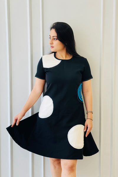 The Dot Women's Dress in black featuring oversized polka-inspired appliqué detailing with a blue braided accent.
